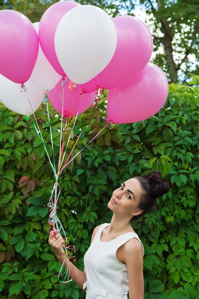 Красивая молодая женщина с воздушными шарами на фоне зеленой изгороди — стоковое фото