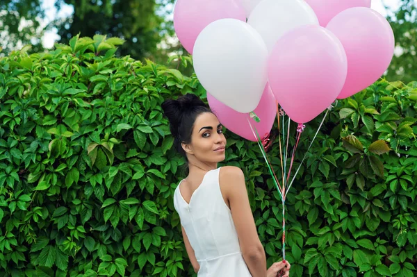 Attraktiva flicka med ballonger som står bredvid en häck — Stockfoto