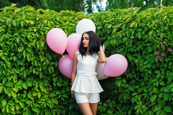 Vacker flicka med ballonger i gröna häckplantor — Stockfoto