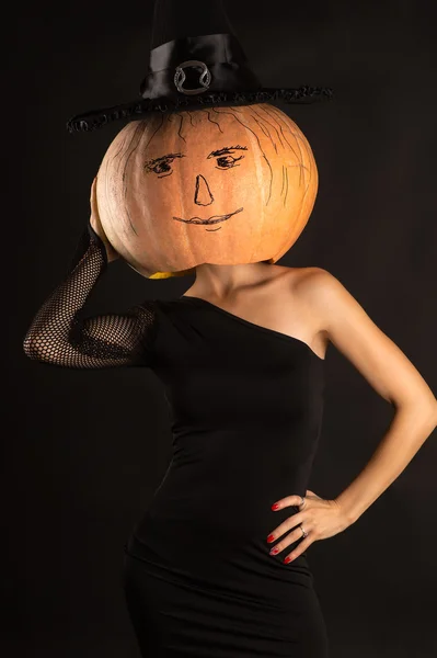 Woman in a black dress with a pumpkin on head in witch hat — Stock Photo, Image