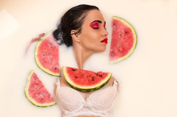 Kvinna med slutna ögon ligga i mjölk med skivor vattenmelon — Stockfoto