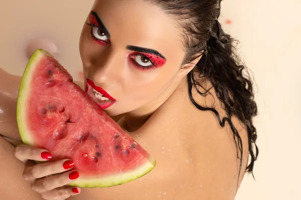 Nassen attraktiven Frau mit hellem Make-up essen Wassermelone sitzt in Milch — Stockfoto