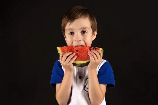 Kleiner Junge isst Wassermelone isoliert auf schwarzem Hintergrund — Stockfoto