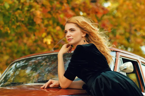 Bella donna bionda con una macchina retrò in autunno — Foto Stock