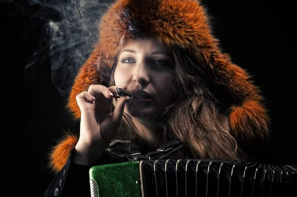 Woman in fur hat with accordion in cigarette smoke — Stock Photo, Image