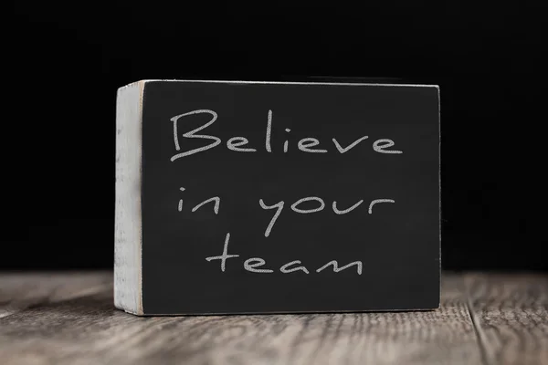 Chalkboard on a wood surface against a black background - Believe in Your Team