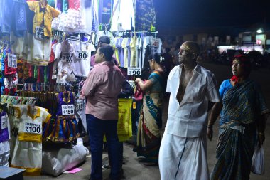 Kanyakumari, Tamil Nadu, Hindistan - Şubat 2017: Hintli Hindu Vaishnavite dindar adam gece Kanyakumari 'de sokak pazarında kumaş satıcısının yanında yürüyor