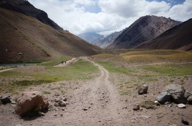 And Dağları doğa yürüyüşü patikasıyla. Ön planda büyük kayalar. Kurak iklim çölleri ve kayalık dağlar. Bulutlardaki Aconcagua Tepesi 'ne bakın. Aconcagua il parkı, Mendoza ili, Arjantin