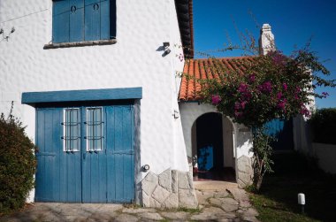 Mar del Plata, Buenos Aires, Arjantin - Mayıs 2020: Beyaz duvarlı, turuncu kiremitli ve mavi panjurlu Akdeniz tarzı ev. Paved avlusu ve çiçek açan ağaç.. 