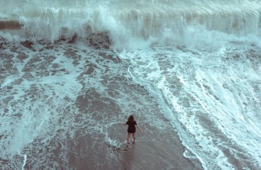 Sahile giden büyük bir gelgit dalgasının önünde tek başına duran bir kadın.