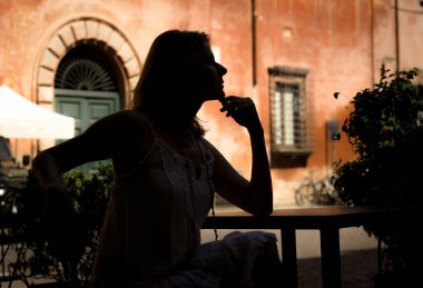 Kafe masasında profilde oturan bir kızın silueti bir Roma caddesinin arka planında 