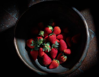 Çilek dolu tabak, antika kasede, bulanık siyah arka planda. 