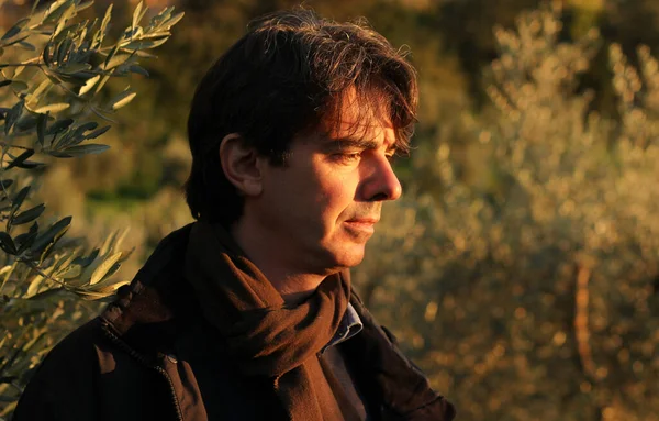 Portrait of a handsome italian man in profile looks at the sunset surrounded by rays of warm light and a garden background