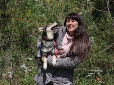 Doğa ve bahar çiçekleriyle çevrili gülümseyen bir köpekle gülümseyen kadın portresi. 