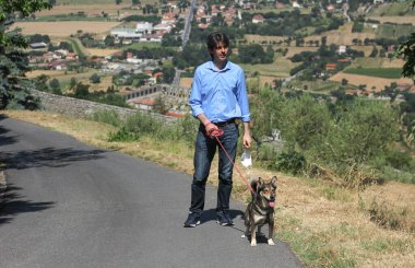 Uzun İtalyan adam Toskana manzarasının arka planında köpeğini gezdiriyor. 