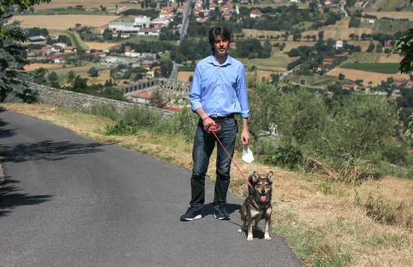 Uzun İtalyan adam Toskana manzarasının arka planında köpeğini gezdiriyor. 