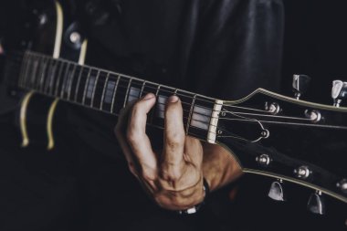 Tişörtlü adam arka planda elektro gitar çalıyor.