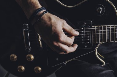 Tişörtlü adam arka planda elektro gitar çalıyor.