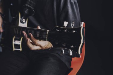 Tişörtlü adam arka planda elektro gitar çalıyor.