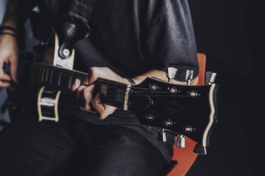 Tişörtlü adam arka planda elektro gitar çalıyor.