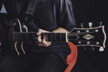 Tişörtlü adam arka planda elektro gitar çalıyor.