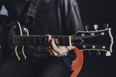 Tişörtlü adam arka planda elektro gitar çalıyor.