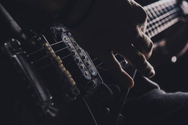 Tişörtlü adam arka planda elektro gitar çalıyor.