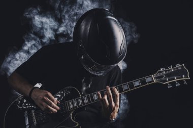 Motosiklet kasklı bir adam arka planda elektro gitar çalıyor.