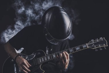 Motosiklet kasklı bir adam arka planda elektro gitar çalıyor.