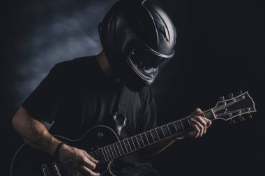 Motosiklet kasklı bir adam arka planda elektro gitar çalıyor.