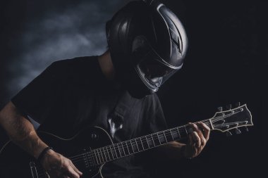 Motosiklet kasklı bir adam arka planda elektro gitar çalıyor.