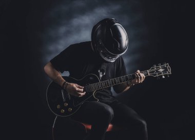 Motosiklet kasklı bir adam arka planda elektro gitar çalıyor.