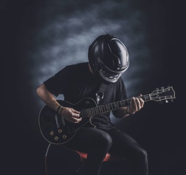 Motosiklet kasklı bir adam arka planda elektro gitar çalıyor.