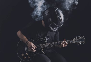 Motosiklet kasklı bir adam arka planda elektro gitar çalıyor.