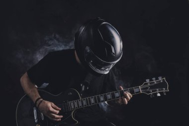 Motosiklet kasklı bir adam arka planda elektro gitar çalıyor.