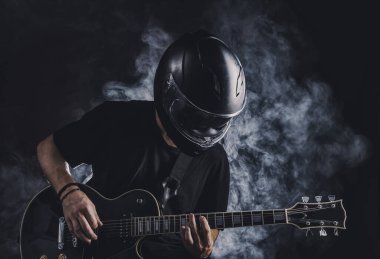 Motosiklet kasklı bir adam arka planda elektro gitar çalıyor.