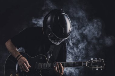Motosiklet kasklı bir adam arka planda elektro gitar çalıyor.
