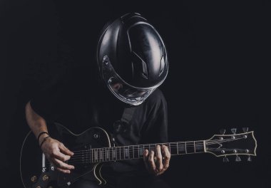 Motosiklet kasklı bir adam arka planda elektro gitar çalıyor.