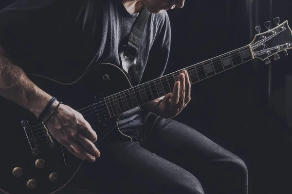 Guy in a T-shirt plays an electric guitar on a dark background