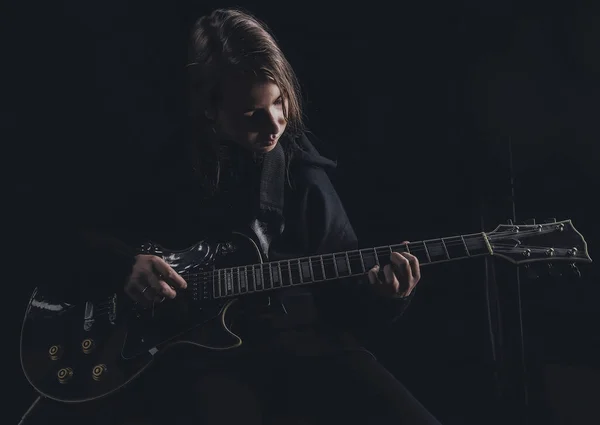 a girl in a black sweatshirt plays an electric guitar on a dark background