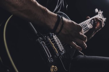 Tişörtlü adam arka planda elektro gitar çalıyor.