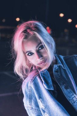 Boş bir otoparkta, gece vakti bir motosikletin üzerinde neon ışıklı bir kızın portresi.
