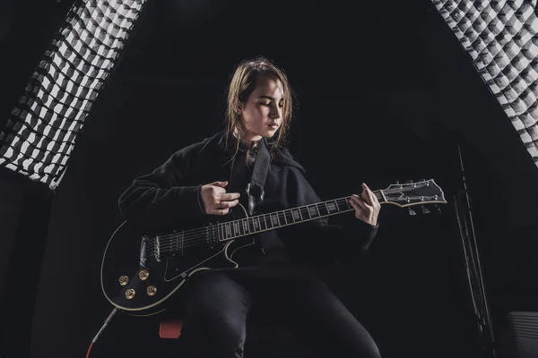 a girl in a black sweatshirt plays an electric guitar on a dark background