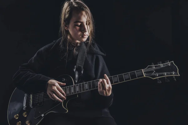 a girl in a black sweatshirt plays an electric guitar on a dark background