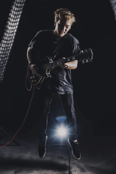 a guy in a dark T-shirt plays an electric guitar in a jump on a dark background