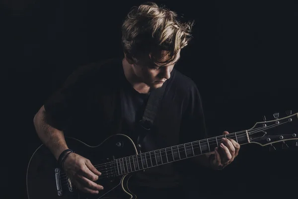 Guy in a T-shirt plays an electric guitar on a dark background