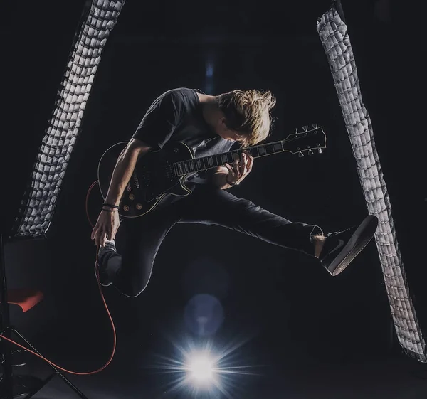 a guy in a dark T-shirt plays an electric guitar in a jump on a dark background