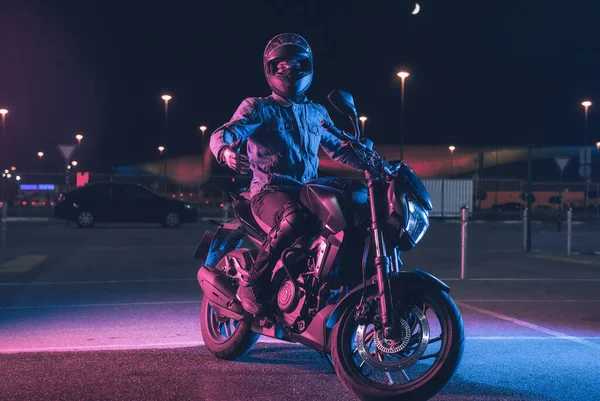 Motorradfahrer Sitzt Nachts Neonlicht Auf Leerem Parkplatz — Stockfoto