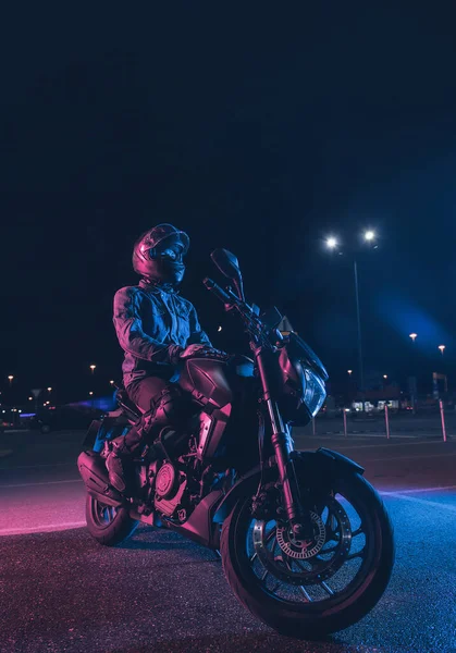 Motorradfahrer Sitzt Nachts Neonlicht Auf Leerem Parkplatz — Stockfoto