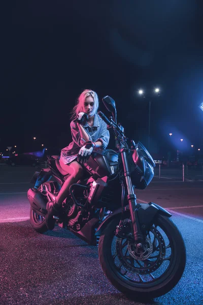在一个空旷的停车场 一个女孩在摩托车上的霓虹灯下的肖像 — 图库照片